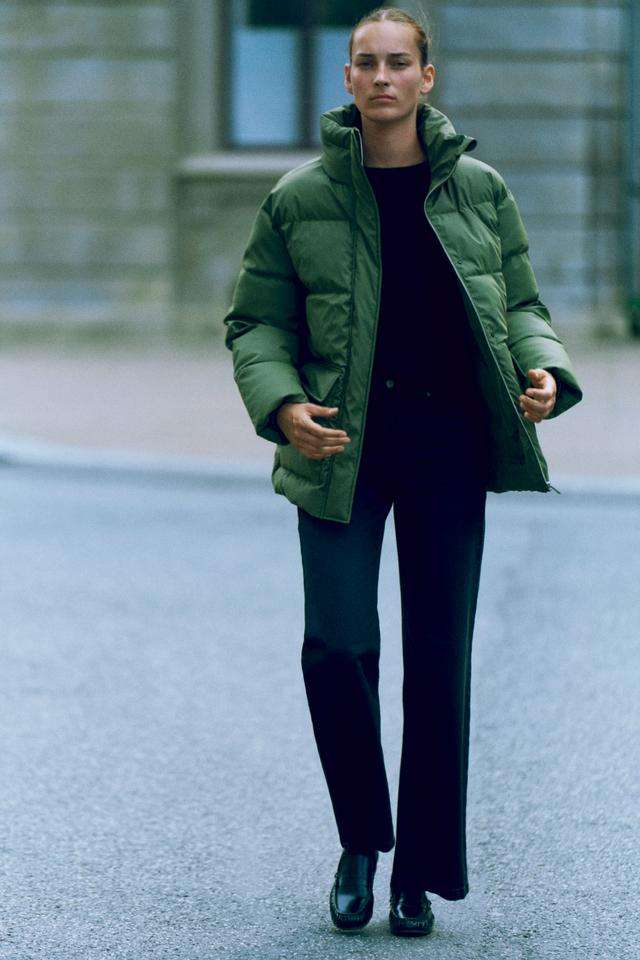 mulher a andar na rua veste calças pretas, camisola preta e blusão acolchoado verde da selected femme portugal